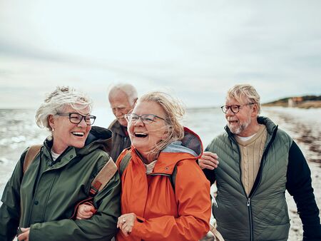 En gruppe seniorer på stranden i blæsevejr, de ser glade ud