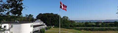 Summer day with hoisting Dannebrog in the garden and a view of the sea