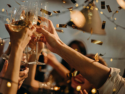 Eine Gruppe stößt auf einer Party mit Champagner zu, während goldenes Konfetti fällt